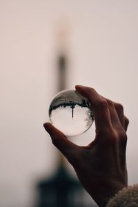 Cropped hand holding crystal ball against white background