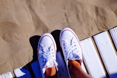 Low section of person wearing white canvas shoes at beach