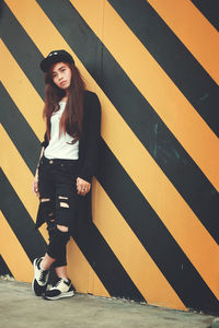 Portrait of young woman standing against striped wall