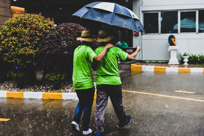 Rear view of friends with umbrella walking on road during rainy season