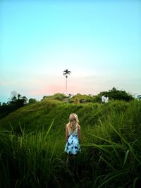 Rear view of woman standing on grassy field against sky