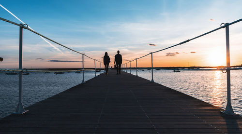 Rear view of silhouette man standing on pier over sea against sky