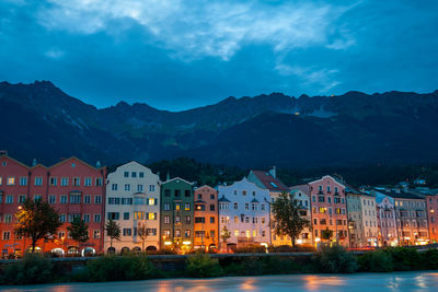 Illuminated buildings by mountains against sky at night