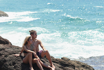 Young couple sitting on the reddish cliffs and looking at the sea of australia