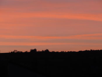 Silhouette trees on field against orange sky