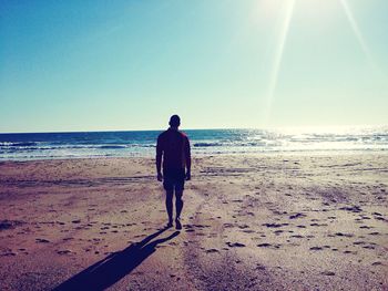 Rear view of man standing on beach against clear sky