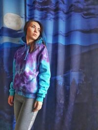 Portrait of young woman standing against curtain