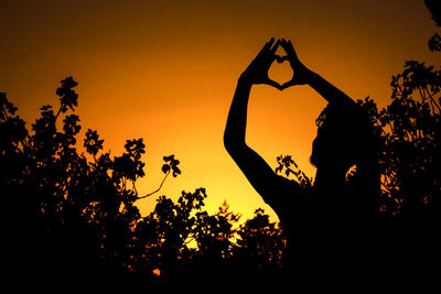 Silhouette woman standing by tree against orange sky