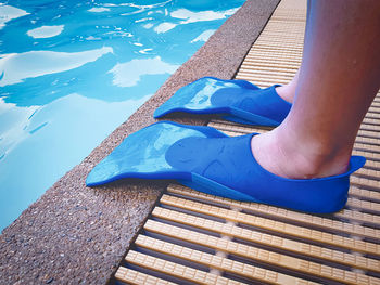 Low section of person wearing diving flippers standing by swimming pool