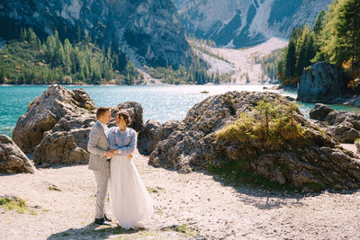 Woman with umbrella on rock by lake against mountains