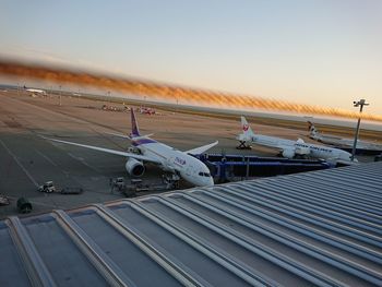 Airplane on airport runway against sky during sunset