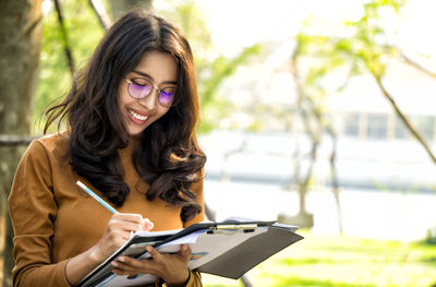 Smiling young woman writing in book outdoors