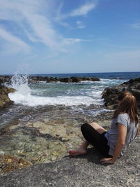 Woman sitting on rock by sea against sky