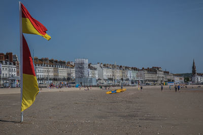 Flag on beach against buildings in city against clear sky