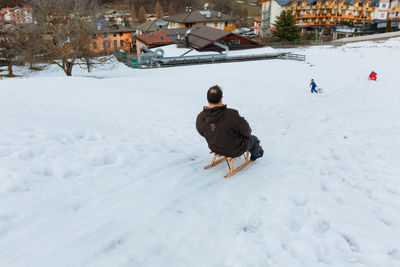 Rear view of man sitting on wooden sled going down the snow hill
