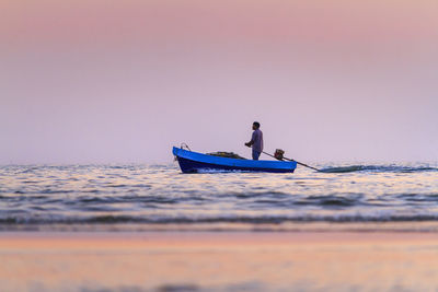 Man on boat in sea against sky during sunset