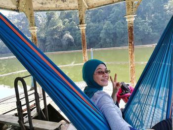 Portrait of smiling woman showing peace sign while relaxing on hammock