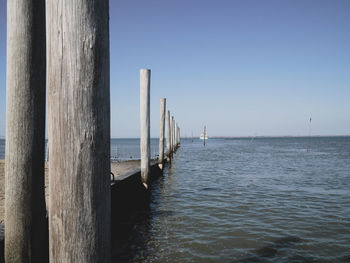 Wooden posts in sea against clear sky