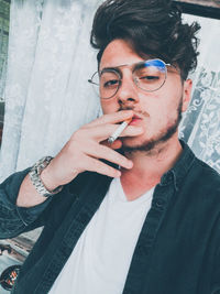 Portrait of young man smoking cigarette against curtain