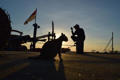 Silhouette man working on road against sky during sunset