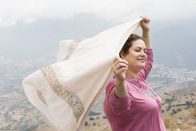 Woman with eyes closed holding aloft scarf while standing on mountain