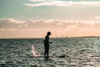 Silhouette man standing in sea against sky during sunset