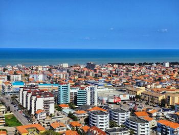 High angle view of townscape by sea against clear blue sky