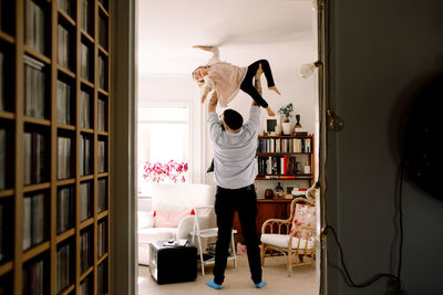 Full length of playful father lifting daughter while standing in living room at home