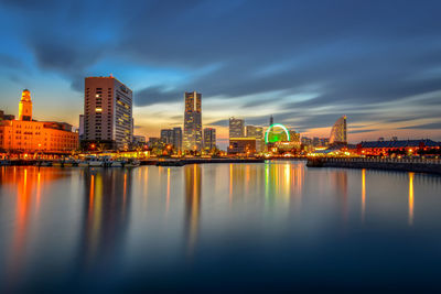 Illuminated buildings by river against sky in city