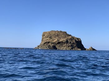 Rock formation in sea against clear blue sky