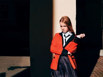 Young woman looking away while standing against wall