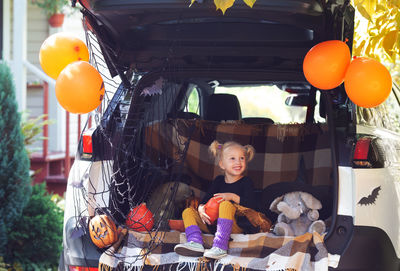 Cute girl sitting in car trunk with halloween equipment
