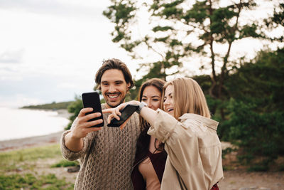 Happy friends taking selfie on smart phone at beach