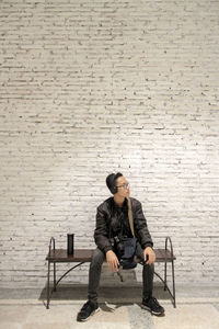 Full length of young man sitting on chair against wall
