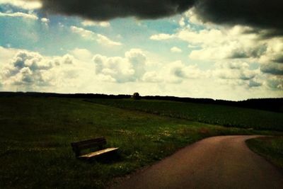 Empty road on grassy field against cloudy sky