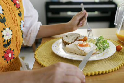 Hands of woman holding table knife and fork by plate on table