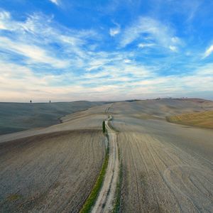 Dirt road passing through desert against sky
