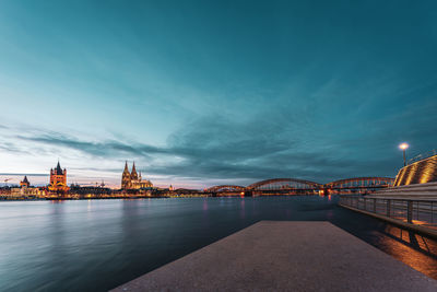 Illuminated bridge over river against cloudy sky