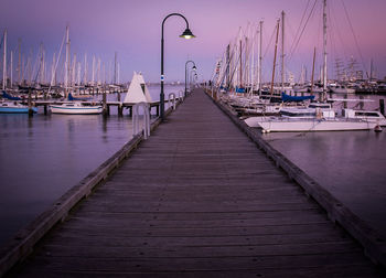 Sailboats moored on pier at harbor against sky