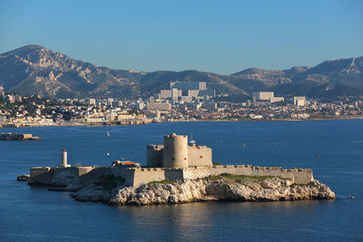 Sea and buildings in city against clear blue sky