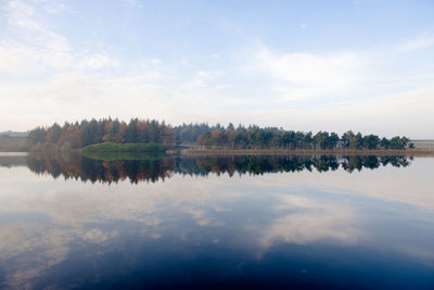 Reflection of wispy sky in shimmery rippled reservoir water. autumn forest along the mid line