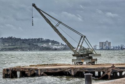 Cranes against pier in sea against sky