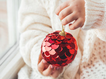 Kid with red decorative ball for christmas tree. boy in cable-knit oversized sweater. 