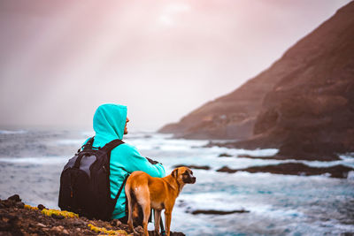 Man with dog sitting on cliff by sea