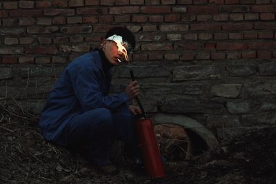 Side view of young man sitting against brick wall