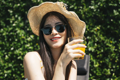 Portrait of young woman holding juice while sitting outdoors