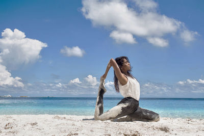 Full length of woman exercising on beach against sky