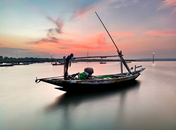 Fishing boat moored in sea against sky during sunset