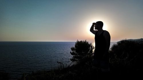 Silhouette man standing by sea against sky