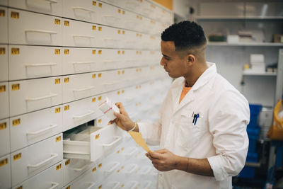 Confident male owner checking medicine from drawer in pharmacy store